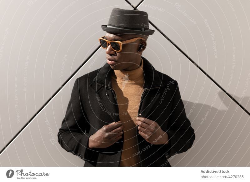 Stilvoller schwarzer Mann vor weißer Wand stehend Outfit selbstbewusst Vorschein trendy cool gut gekleidet Hut Sonnenbrille Individualität Persönlichkeit modern