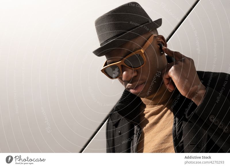 Stilvoller schwarzer Mann vor weißer Wand stehend Outfit selbstbewusst Vorschein trendy cool gut gekleidet Hut Sonnenbrille Individualität Persönlichkeit modern