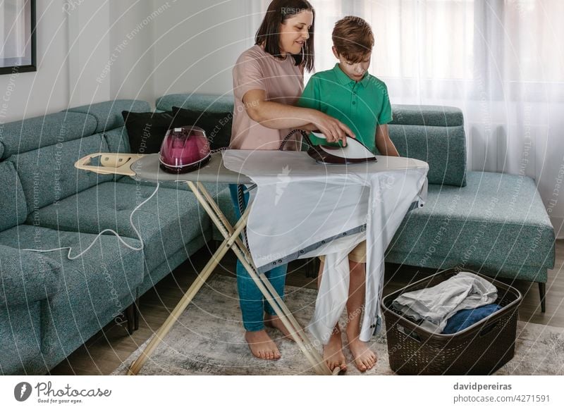 Mutter lehrt ihren Teenager-Sohn zu bügeln Lehre bügelnd heimwärts Hilfe Bügelbrett Wäschekorb Kleidung Zusammensein Wohnzimmer Hausfrau Kind Frau Menschen