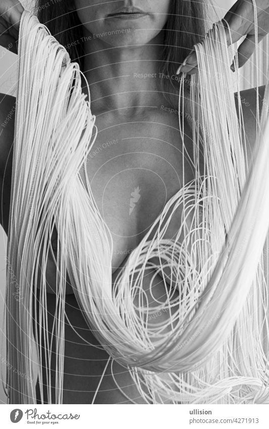 Attraktiver, sexy Körper, Kinn und Mund einer jungen, hinreißenden Frau, teilweise verdeckt von den weißen Fäden eines fallenden Fadenvorhangs, der in eleganten Formen dekoriert ist.