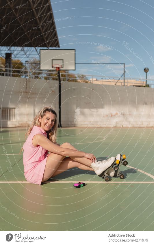 Glückliche Frau in Rollschuhen auf einem Sportplatz sitzend Zahnfarbenes Lächeln Skater Rolle Sportpark heiter Aktivität Hobby sportlich Energie Inhalt
