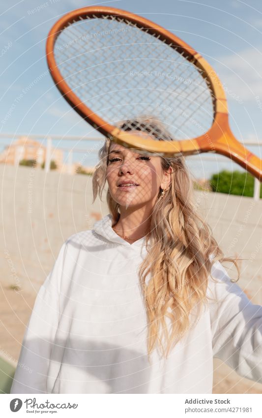Attraktive Frau schaut durch einen Tennisschläger auf der Straße in die Kamera Remmidemmi positiv froh sportlich Gerät jung Inhalt Lifestyle sorgenfrei angenehm