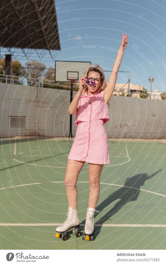 Fröhliche Frau auf Rollschuhen beim Fotografieren mit einer Sofortbildkamera Skater fotografieren Rolle heiter Arm angehoben Sportpark Aktivität Hobby Stil