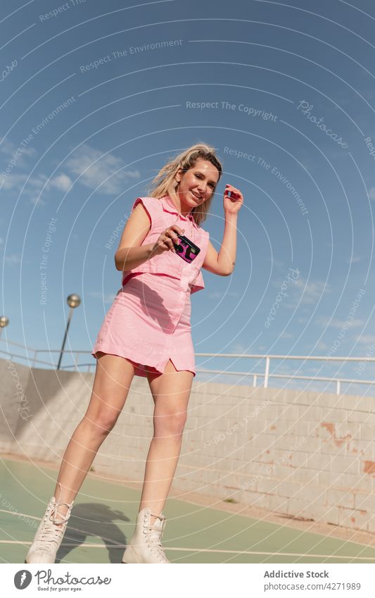 Fröhliche Frau auf Rollschuhen beim Fotografieren mit einer Sofortbildkamera Skater fotografieren Rolle heiter Sportpark Aktivität Hobby Stil blond Gedächtnis