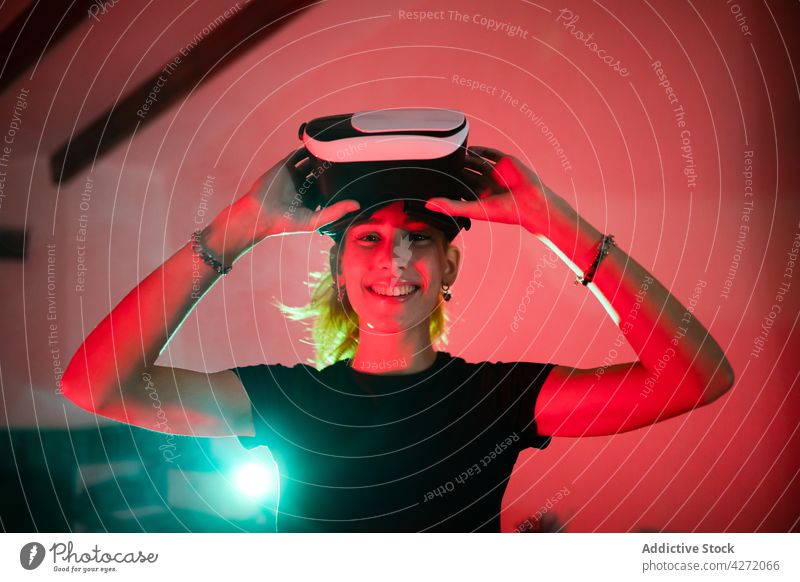 Lächelnde Frau mit VR-Brille in neonfarbenem Raum modern Headset Atelier neonfarbig Virtuelle Realität rot Licht Schutzbrille Gerät Apparatur virtuell Erfahrung