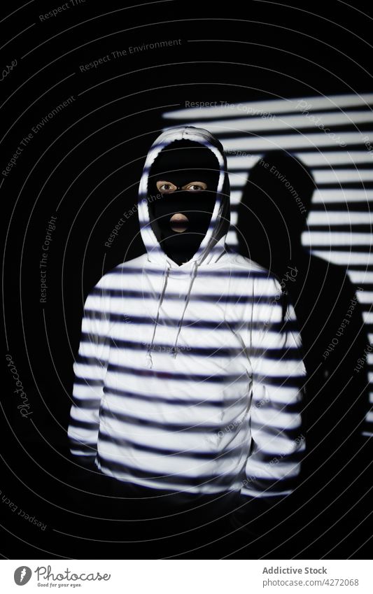 Anonymer rebellischer Mann in Kapuzenpulli und Gesichtsmaske, der in der Nähe einer Mauer steht auflehnen Sturmhaube Mundschutz inkognito ernst nachdenklich