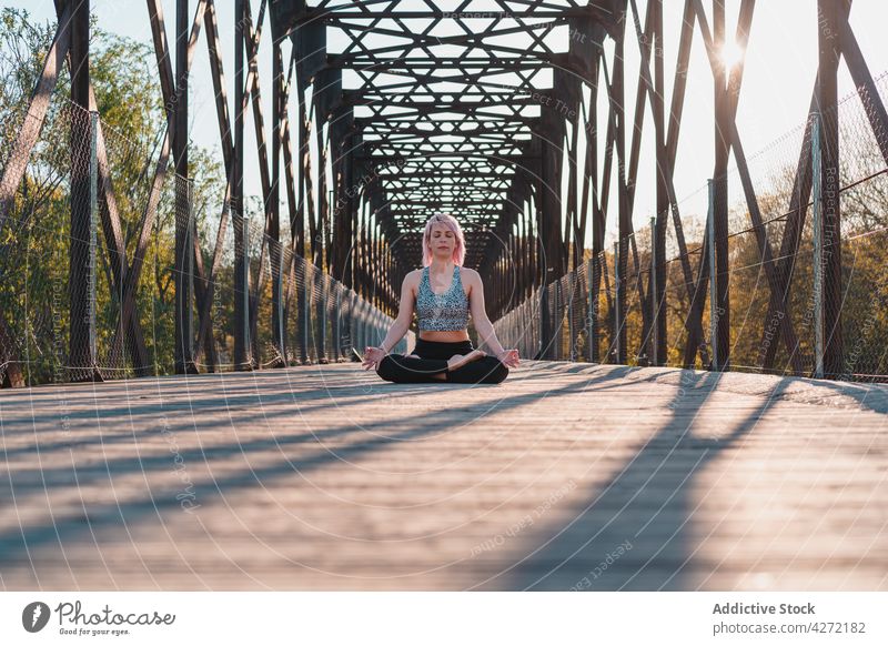 Frau meditiert in Lotus-Pose auf einer Brücke im Sonnenschein meditieren Yoga Sprit Stressabbau Energie Harmonie Mudra Fußweg Augen geschlossen idyllisch