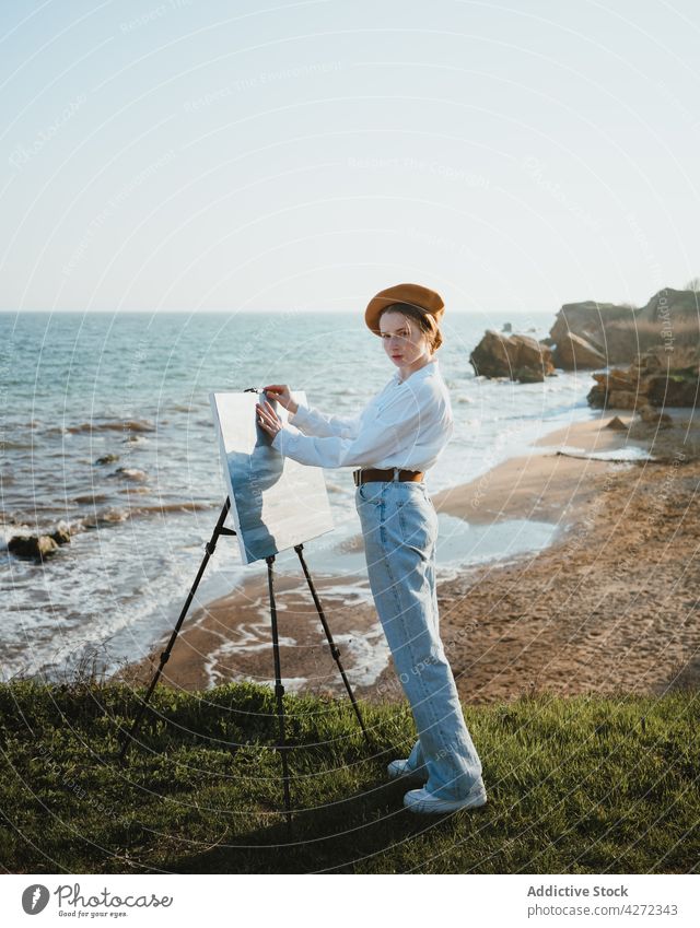 Künstlerin am Ufer bei Sand und Meer beim Malen Frau Farbe zeichnen Hobby MEER Kunst Leinwand jung Staffelei Baskenmütze kreativ Kunstwerk Stil weißes Hemd