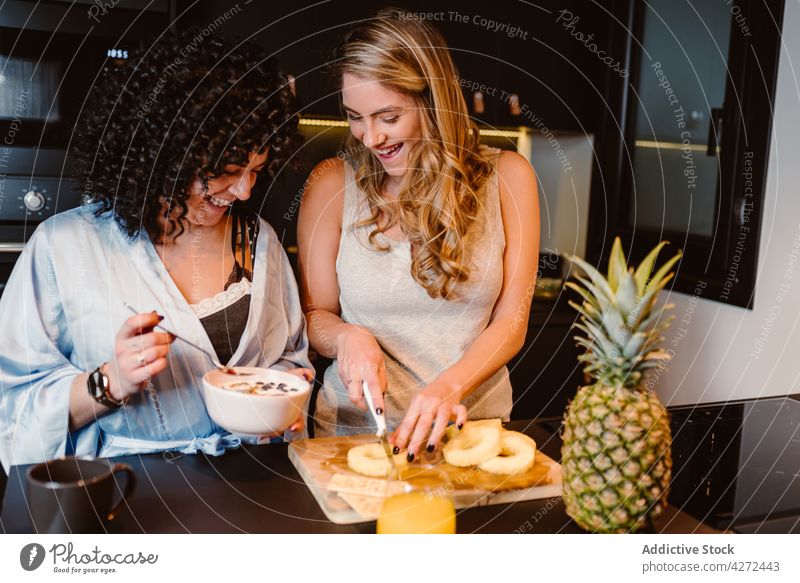 Glückliche Freundinnen haben Spaß am Morgen in der Küche Frauen Paar Lachen geschnitten Ananas Freude Frühstück lgbt Müsli Vergnügen lesbisch heiter Beeren