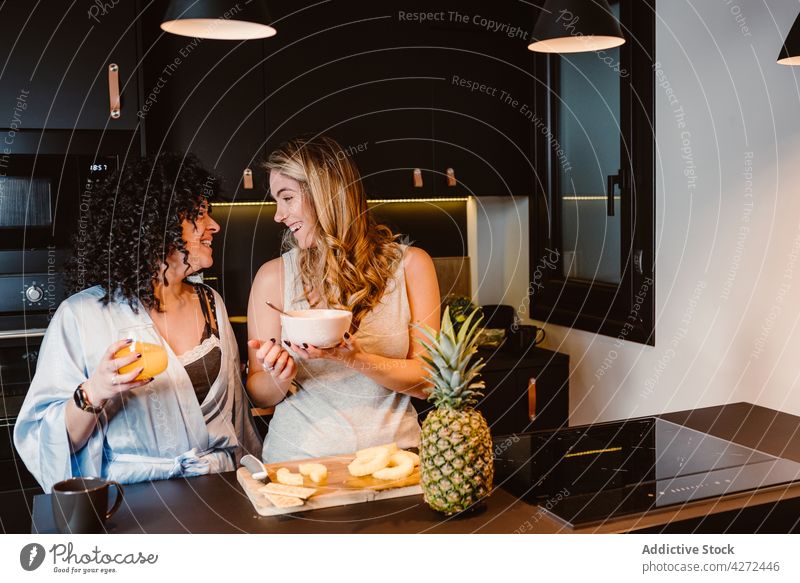 Glückliche Freundinnen haben Spaß am Morgen in der Küche Frauen Paar Lachen geschnitten Ananas Freude Frühstück lgbt Müsli Vergnügen lesbisch heiter Beeren