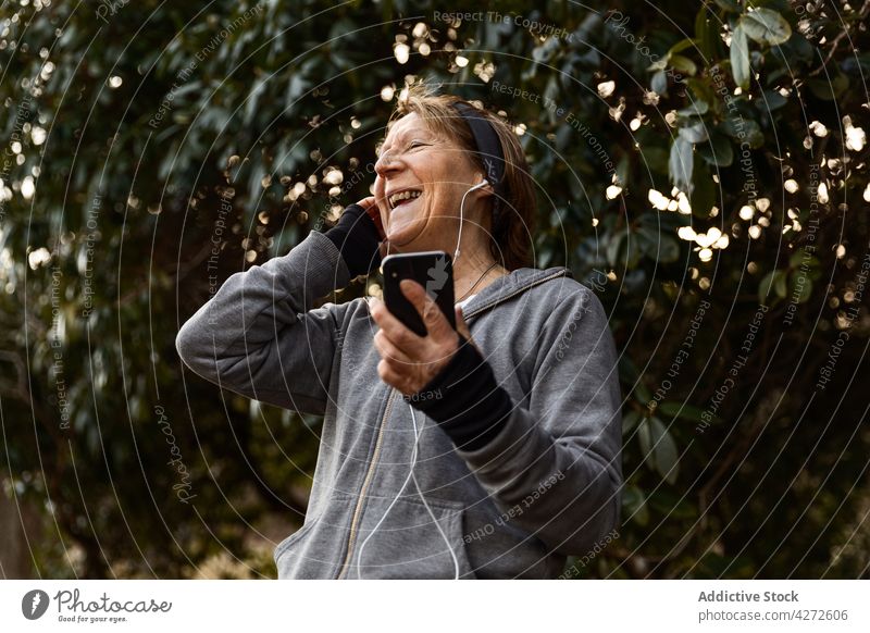Positive ältere Frau, die während des Trainings Musik auf ihrem Smartphone hört gealtert zuhören benutzend Fitness Kopfhörer positiv Sportbekleidung Gerät