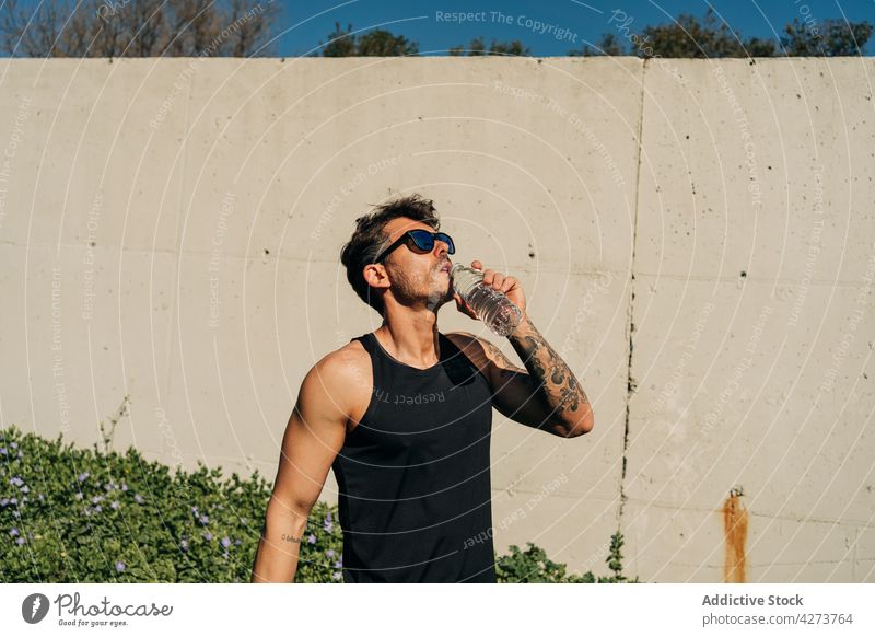 Sportler trinkt Wasser nach dem Training in der Stadt Athlet trinken durstig Erfrischung sportlich maskulin Tattoo muskulös Mann Flasche Sonnenbrille genießen