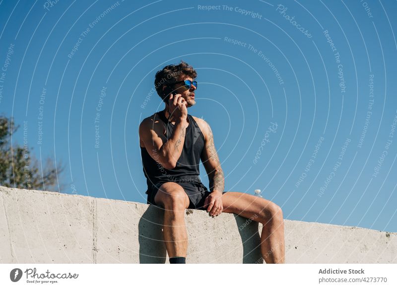 Sportler spricht am Zaun in der Stadt mit seinem Smartphone reden sprechen Stimme freie Zeit Pause benutzend Apparatur Mann Gerät Funktelefon Schatten sitzen