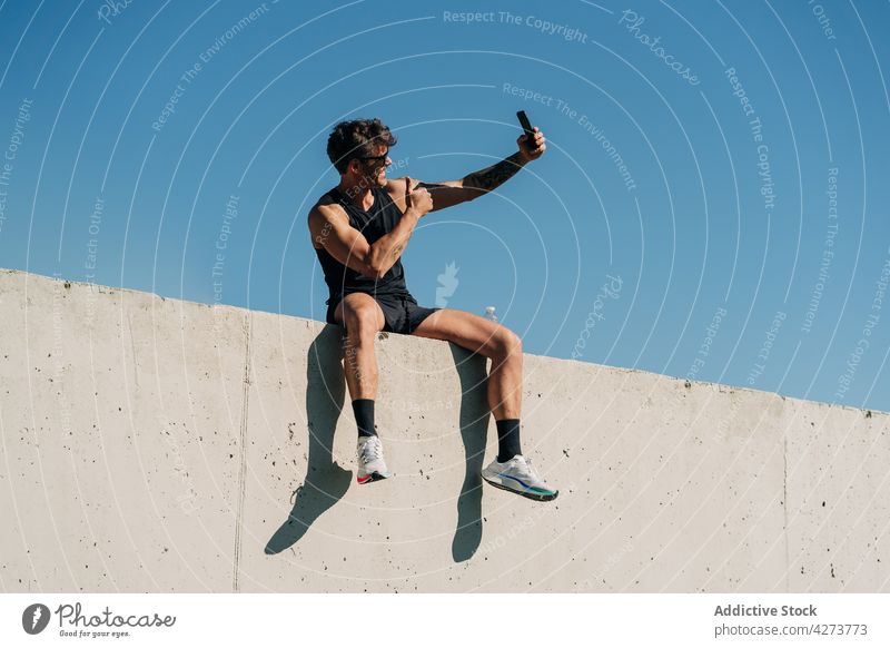 Sportler macht Selfie am Zaun in der Stadt Smartphone unter freie Zeit Pause benutzend Apparatur Mann Gerät Funktelefon Schatten sitzen Park Kommunizieren