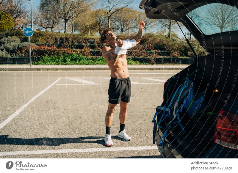 Muskulöser Sportler beim Anziehen eines T-Shirts gegen ein Auto angezogen Unterleib sportlich maskulin Macho PKW parken Straßenbelag Großstadt Mann Stadt
