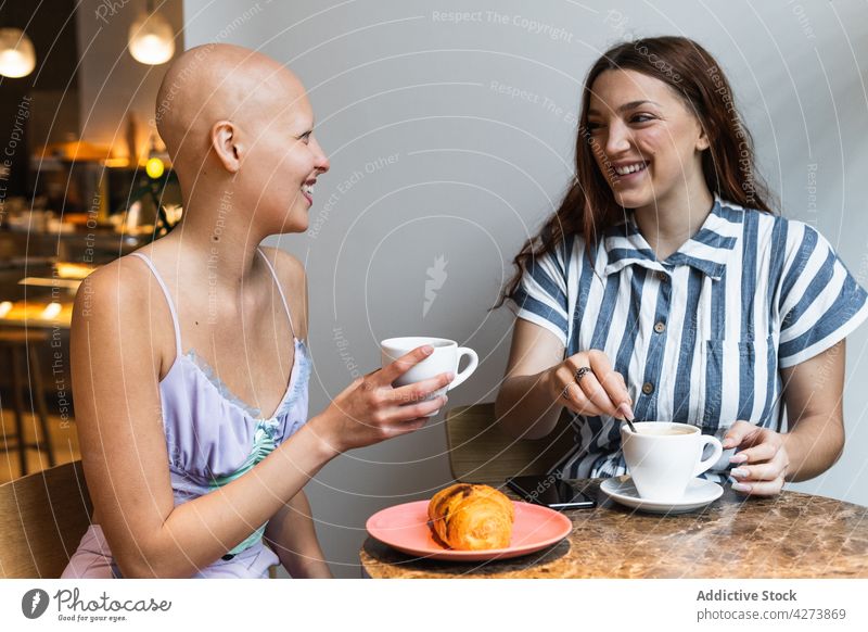Fröhliche junge Freundinnen, die Spaß haben, während sie ein Croissant essen und Kaffee in einem Café trinken Frauen Kaffeepause Lachen Freude positiv genießen