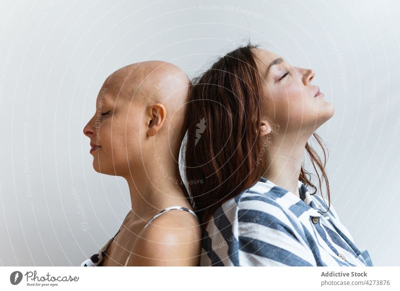 Junge Freundinnen stehen Rücken an Rücken mit geschlossenen Augen Frauen Augen geschlossen bester Freund Alopezie Problematik abstützen Zusammensein