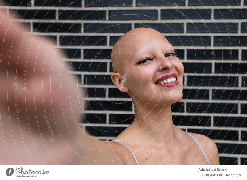 Lächelnde glatzköpfige Frau nimmt Selfie auf Telefon in der Nähe von Backsteinmauer Smartphone Backsteinwand kahl Straße modern Glück jung Gerät Mobile