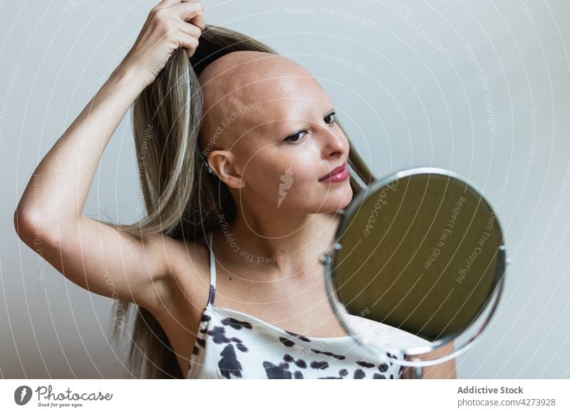 Junge Frau nimmt ihre Perücke ab und schaut in den Spiegel selbstbewusst Abheben Alopezie Krankheit Vorschein Persönlichkeit feminin Individualität Make-up jung