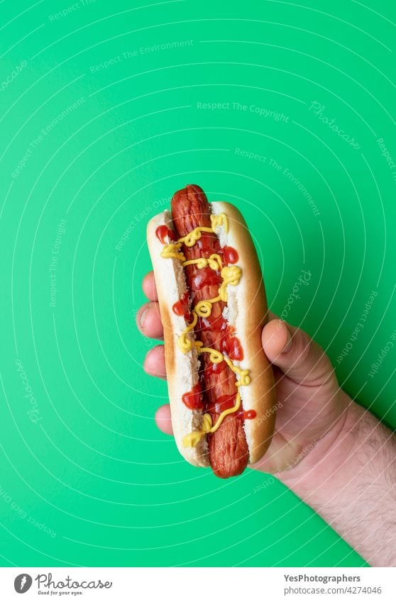 Hot Dog in Männerhand auf einem grünen Tisch, Ansicht von oben. Amerikaner Arme Hintergrund Brot Brötchen Kalorien Farbe Textfreiraum Küche ausschneiden lecker