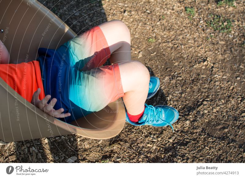Am Ende der Rutsche: Junge verlässt eine Röhrenrutsche mit bunter Kleidung und Schuhen Sliden Tube Regenbogen Spielplatz Aufstieg Park Gerät Schulpause