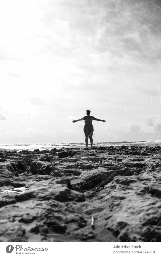 Anonyme Frau hebt die Hände am felsigen Ufer in der Nähe des Ozeans MEER Meer Felsen Arme hochgezogen Übergröße allein bw mollig sonnig schwarz auf weiß Cloud