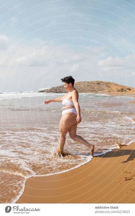 Frau steht am Sandstrand im Meer MEER Strand Übergröße Badeanzug Blauer Himmel Spaß haben Ufer allein jung schäumen Tourist Meeresufer Harmonie tagsüber Wasser