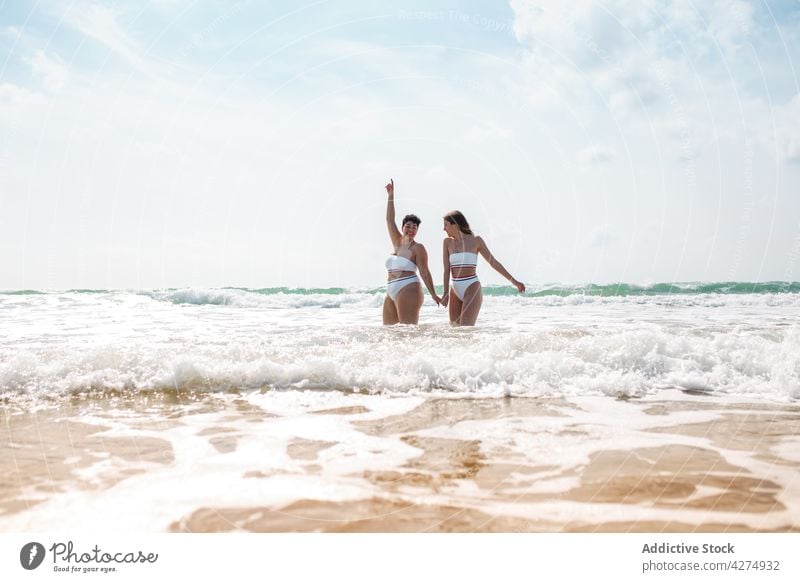 Damen im Meer stehend in der Nähe der sandigen Küste Frauen Freund Spaß haben Strand Lächeln Sand Badeanzug Blauer Himmel Glück aqua Händchenhalten Meeresufer