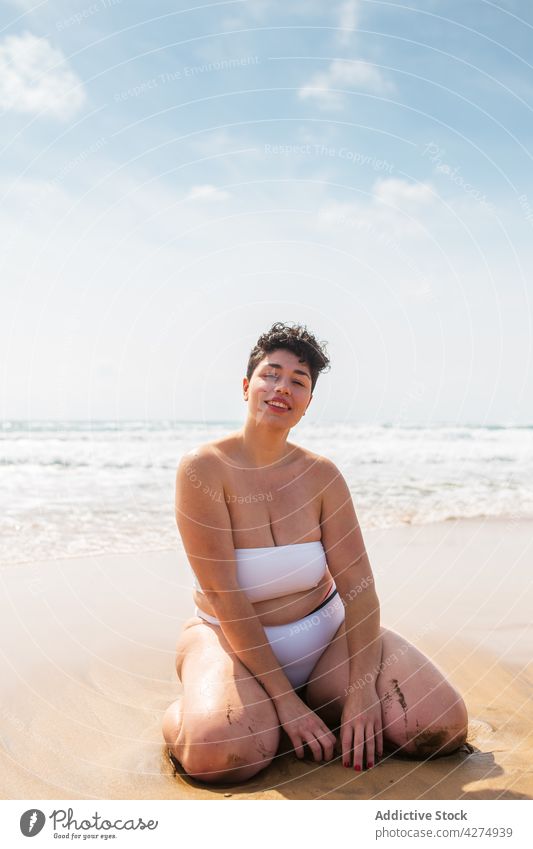 Frau sitzt am Sandstrand in der Nähe des Meeres Strand Lächeln Übergröße Badeanzug Urlaub Blauer Himmel Glück jung aqua genießen MEER allein hell Freude
