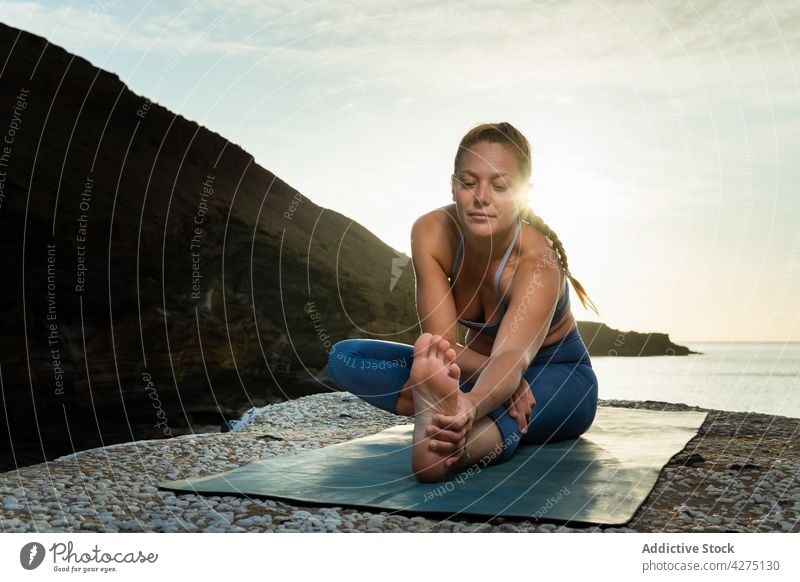 Frau in Vorwärtsbeuge auf Yogamatte gegen das Meer Dehnung Hände gefaltet Füße berühren Konzentration Meeresufer Sonnenschein Kieselsteine Gesunder Lebensstil