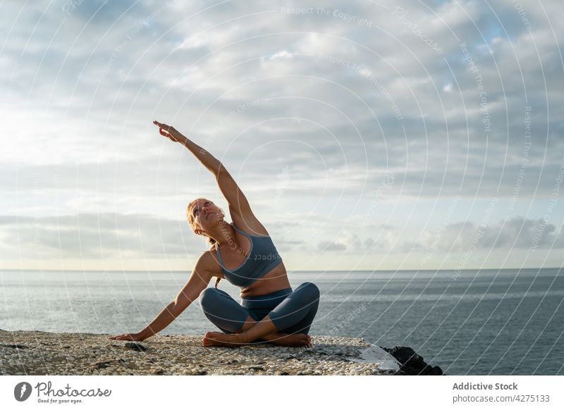 Frau übt Yoga mit erhobenem Arm am Meeresufer üben Beine gekreuzt Arm angehoben Seitenknick Vitalität Wellness Küste Abend Gesunder Lebensstil Wohlbefinden