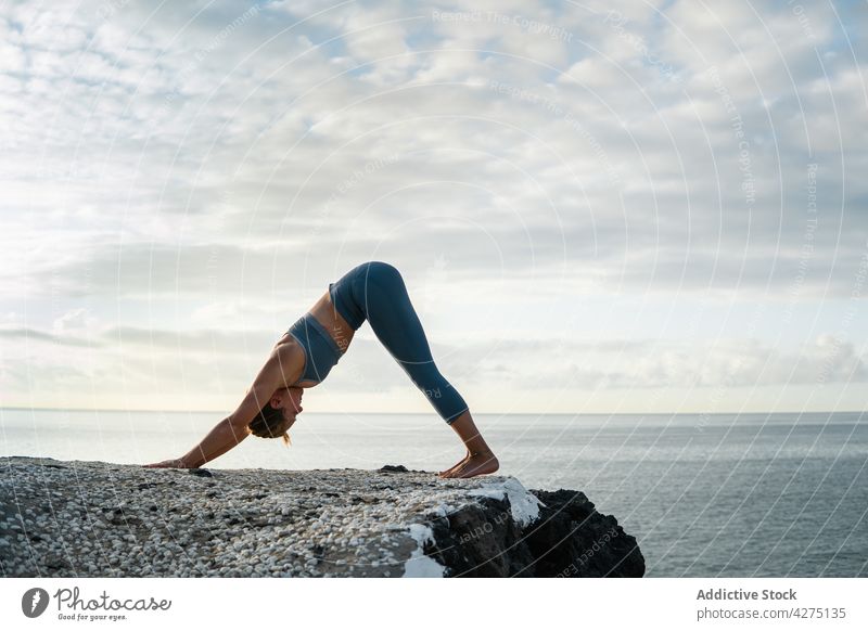 Flexible Frau zeigt Downward Facing Dog Pose gegen das Meer Yoga nach unten gerichteter Hund Dehnung beweglich Vorwärtsbeuge Gesunder Lebensstil Vitalität MEER