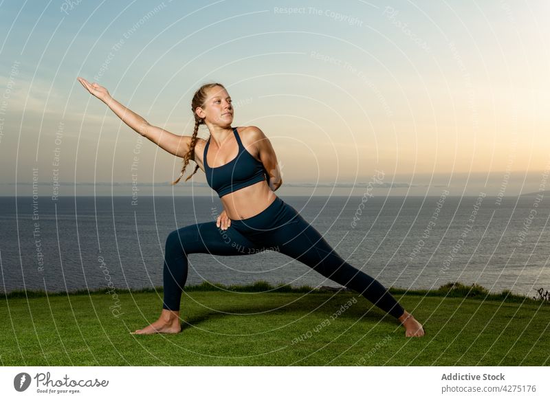 Frau in Halbmond-Longe-Pose am Meeresufer halbmondförmiger Ausfallschritt Yoga ausdehnen beweglich Wellness Gesunder Lebensstil Oberschenkel anfassen Abend