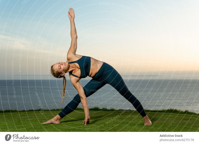 Frau in Dreieckspose am Meeresufer Yoga ausdehnen beweglich Triangel-Pose Wellness Gesunder Lebensstil trikonasana Abend Gras üben Dehnung MEER Gleichgewicht