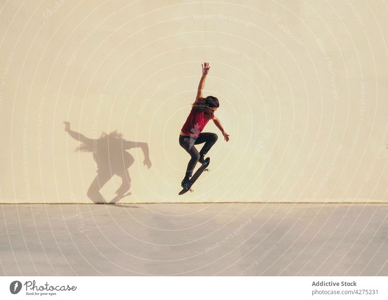 Aktiver Skater springt mit Skateboard auf beigem Hintergrund Skateboarderin springen Trick Sport aktiv Gleichgewicht Energie dynamisch Mann schnell ausdehnen