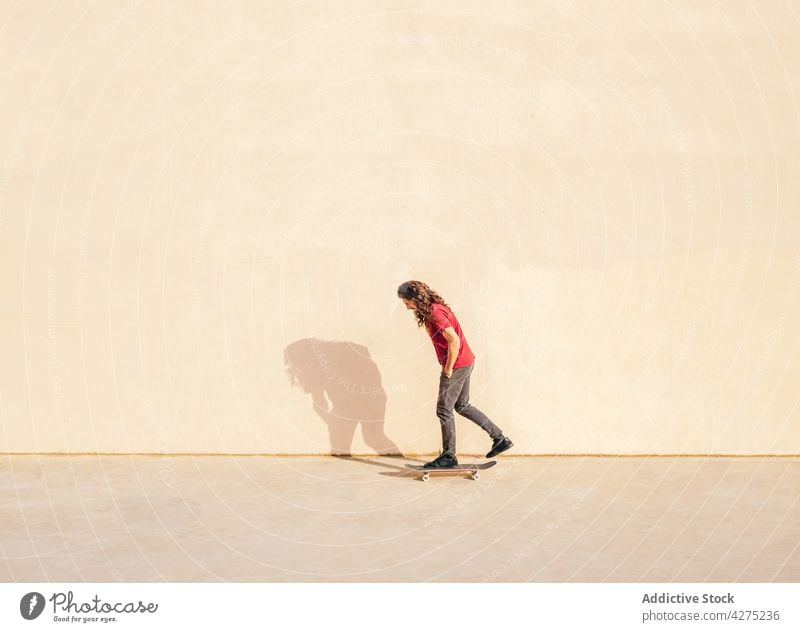 Skater auf Skateboard gegen Wand mit Schatten im Freien Hand-in-Tasche Sport nachdenken Lifestyle Mann Einsamkeit Straßenbelag bewundern Laufsteg stehen einsam