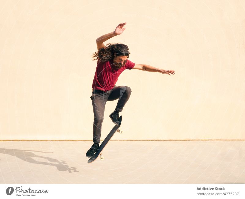 Aktiver Skater springt mit Skateboard auf beigem Hintergrund Skateboarderin springen Trick Sport aktiv Gleichgewicht Energie dynamisch Mann schnell ausdehnen