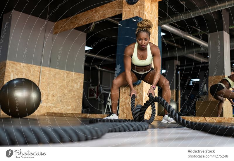 Entschlossene schwarze Sportlerin beim Training mit schweren Seilen in einer Turnhalle Schlacht operativ Fitness Motivation Stärke Herz Fitnessstudio Kraft Frau