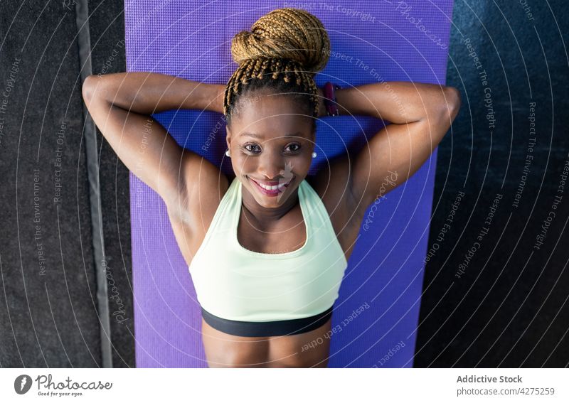 Lächelnde schwarze Sportlerin beim Training auf einer Matte im Fitnessstudio Athlet heiter Hand hinter dem Kopf Übung Frau Unterlage Porträt stark Körper