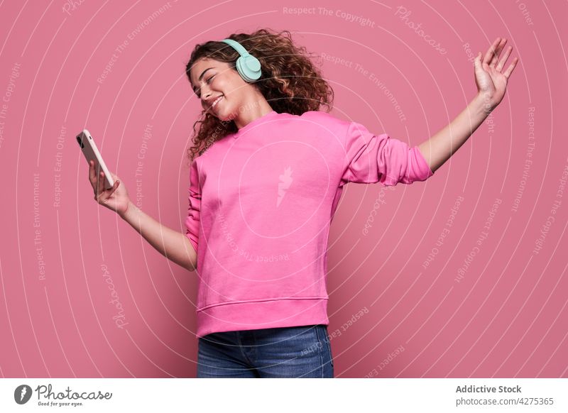 Lächelnde Frau, die Musik hört und ein Smartphone benutzt zuhören benutzend Kopfhörer springen genießen lebhaft cool Glück heiter Teenager Vergnügen Gerät