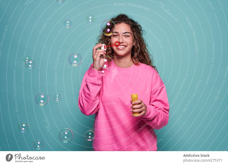 Entzückte Frau beim Blasen von Seifenblasen im Studio Schlag Spaß Lachen Vergnügen Teenager Freude spielerisch lebhaft Schaumblase heiter Optimist froh