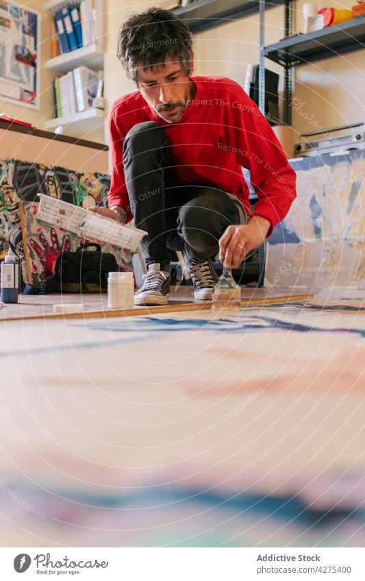 Aufmerksamer Künstler beim Malen von Kunstwerken mit Pinsel in einer Werkstatt Farbe Pinselblume achtsam Talent Fähigkeit Mann Prozess Fokus lässig anhaben Stil
