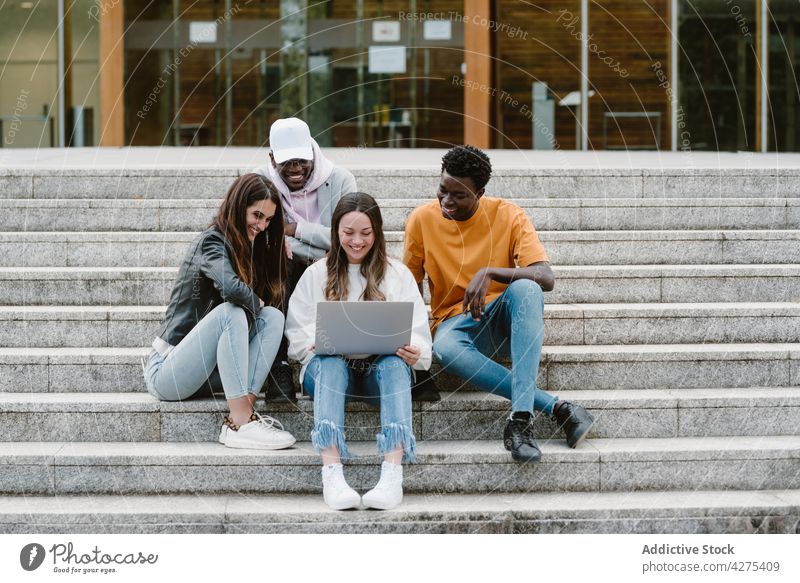Multiethnische Studenten benutzen Laptop auf den Stufen der Universität Männer Frauen Freund zuschauen benutzend Internet teilen froh genießen männlich