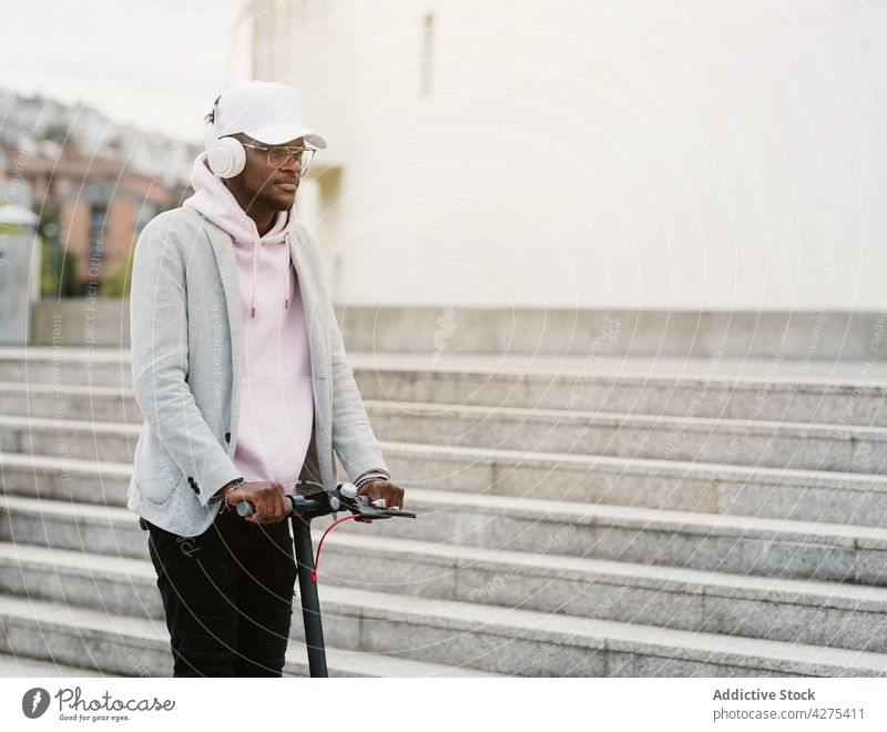 Schwarzer Mann fährt Elektroroller im Park Kopfhörer Musik nachdenklich zuhören elektrisch Mitfahrgelegenheit Tretroller Drahtlos positiv Freizeit männlich