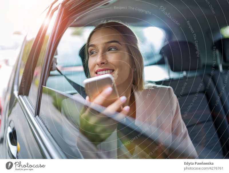 Junge Frau mit Smartphone auf dem Rücksitz eines Autos Carsharing selbstbewusst Lächeln Befriedigung attraktiv schön junger Erwachsener Freude positiv Inhalt