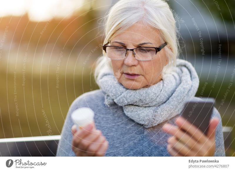 Frau hält Smartphone und Pillenflasche Senior Senioren Rentnerin Rentnerinnen lässig im Freien eine Person in den Ruhestand getreten außerhalb gealtert Alterung