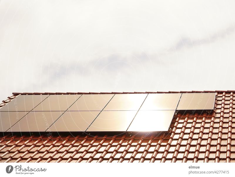 In den elf Sonnenkollektoren auf dem roten Ziegeldach eines Wohnhauses spiegelt sich die Sonne / Stromerzeugung / Ökostrom / Photovoltaikanlage Kollektoren