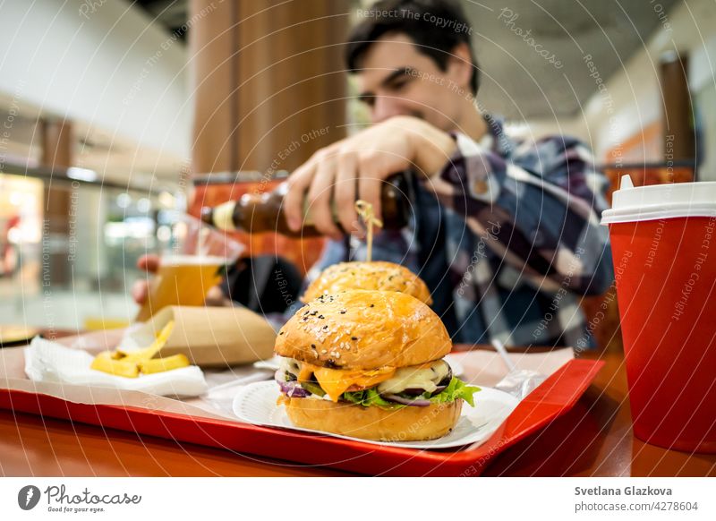 Mann isst Fastfood-Burger und trinkt Bier allein im offenen Bereich eines Restaurants in einem Einkaufszentrum Mahlzeit Lebensmittel Bar Glück Pub essen schnell