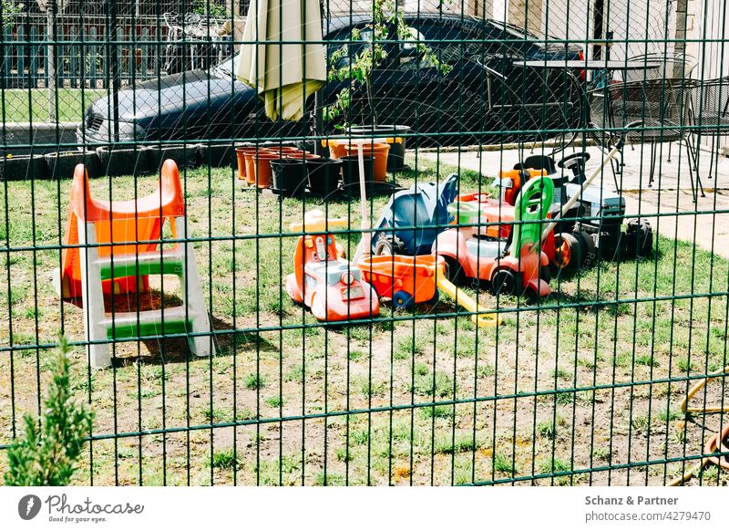bunte Spielfahrzeuge im Garten Spielsachen Plastik Zaun Fuhrpark Fahrzeuge spielen Lockdown Privatsphäre Wiese Gras Rasen Außenaufnahme Spielen Kontaktsperre
