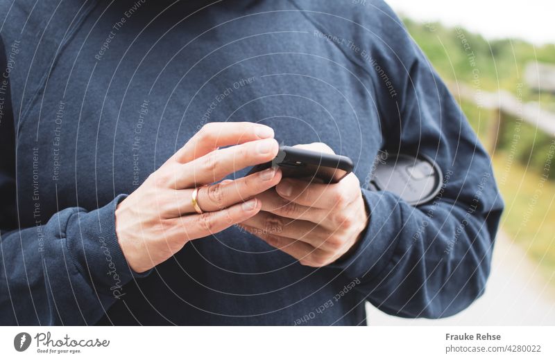 Nahaufnahme eines Mannes mit einem Kaffeebecher unterm Arm, der mit einem schwarzen Smartphone beschäftigt mobiles Arbeiten Hände Handy Technik & Technologie